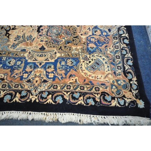 1300 - A LARGE WOOLLEN CREAM GROUND RUG, with a repeating foliate pattern, within a dark blue field, and a ... 