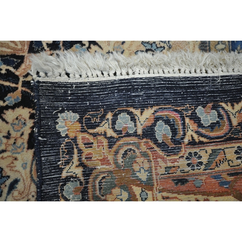 1300 - A LARGE WOOLLEN CREAM GROUND RUG, with a repeating foliate pattern, within a dark blue field, and a ... 