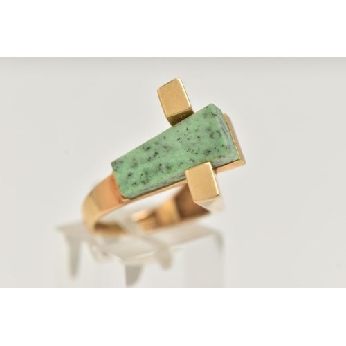 53 - A YELLOW METAL GEM SET DRESS RING, designed with a tapered slice of green hardstone, between two pol... 