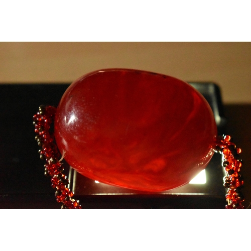 153 - A SMALL BAG OF ITEMS, to include a large oval cherry amber colour Bakelite bead fitted on a red bead... 