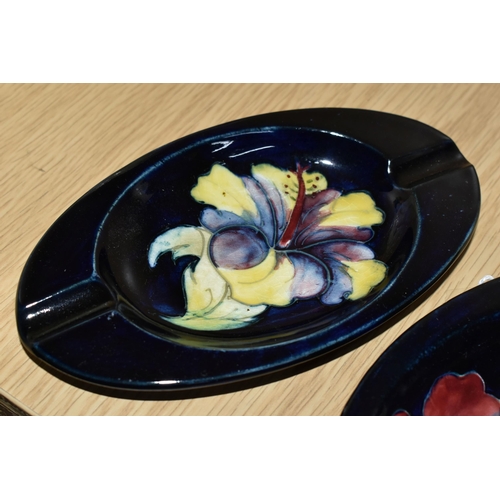 474 - TWO MOORCROFT POTTERY 'HIBISCUS' PATTERN ASHTRAYS, one of teardrop shape, tube lined with a pink/pur... 