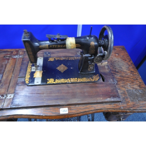 1284 - AN EARLY 20TH CENTURY STERLING TREADLE SEWING TABLE, with an oak case, four drawers, raised on a cas... 