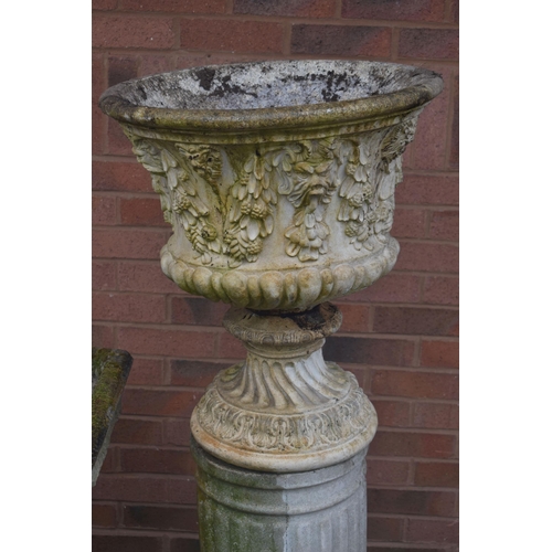 1007 - A WEATHERED COMPOSITE GARDEN URN, depicting masks and flowers with swag, on an odd Reeded cylindrica... 