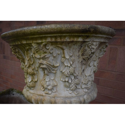 1007 - A WEATHERED COMPOSITE GARDEN URN, depicting masks and flowers with swag, on an odd Reeded cylindrica... 