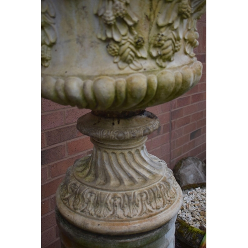 1007 - A WEATHERED COMPOSITE GARDEN URN, depicting masks and flowers with swag, on an odd Reeded cylindrica... 