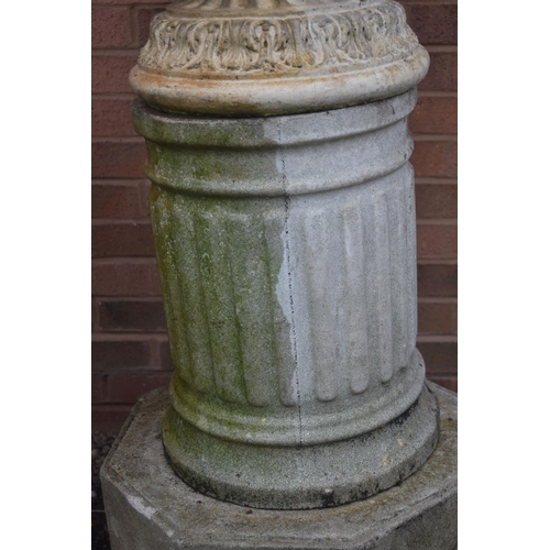 1007 - A WEATHERED COMPOSITE GARDEN URN, depicting masks and flowers with swag, on an odd Reeded cylindrica... 