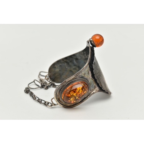 33 - A LARGE WHITE METAL AND COPAL AMBER BRACELET, designed as a horse saddle, fitted with chain stirrups... 