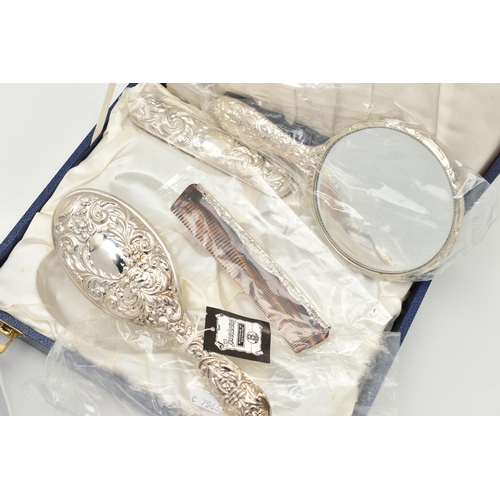 84 - A CASED SILVER MOUNTED DRESSING TABLE SET, to include two brushes, a mirror and comb, with embossed ... 