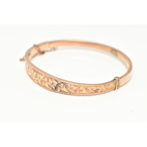 87 - AN EDWARDIAN 9CT GOLD HINGED BANGLE, the front designed as a foliate engraved tapering hollow panel,... 