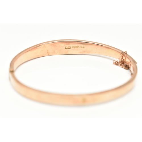 87 - AN EDWARDIAN 9CT GOLD HINGED BANGLE, the front designed as a foliate engraved tapering hollow panel,... 