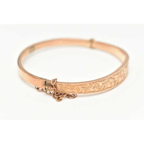 87 - AN EDWARDIAN 9CT GOLD HINGED BANGLE, the front designed as a foliate engraved tapering hollow panel,... 