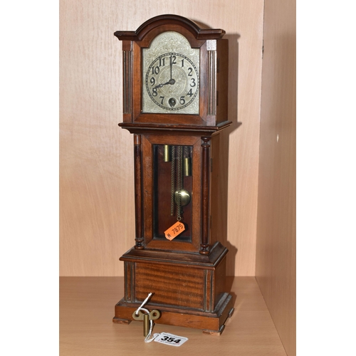 354 - A MANTEL CLOCK IN THE FORM OF A GRANDFATHER CLOCK, with black Arabic numerals on a painted metal dia... 