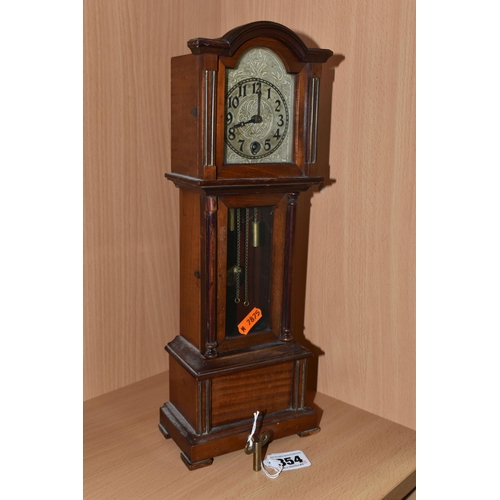 354 - A MANTEL CLOCK IN THE FORM OF A GRANDFATHER CLOCK, with black Arabic numerals on a painted metal dia... 