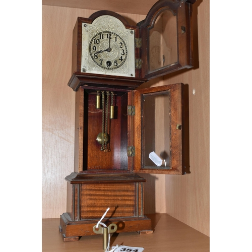 354 - A MANTEL CLOCK IN THE FORM OF A GRANDFATHER CLOCK, with black Arabic numerals on a painted metal dia... 