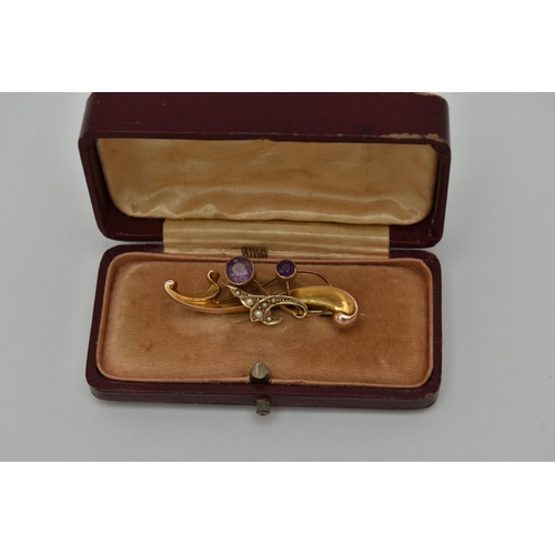 22 - AN EARLY 20TH CENTURY BROOCH, a scrolling yellow gold brooch set with two circular cut amethysts and... 