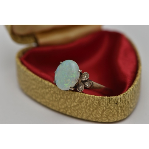 23 - AN OPAL RING, an oval opal, approximate length 10.5mm, prong set in white metal, flanked with six si... 