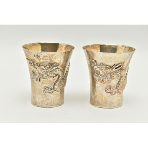 89 - A PAIR OF WHITE METAL ORIENTAL CUPS, each decorated with dragons, stamped to the base 'Silver', with... 