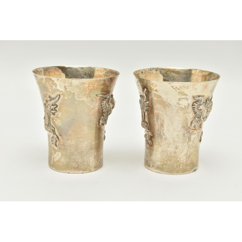 89 - A PAIR OF WHITE METAL ORIENTAL CUPS, each decorated with dragons, stamped to the base 'Silver', with... 