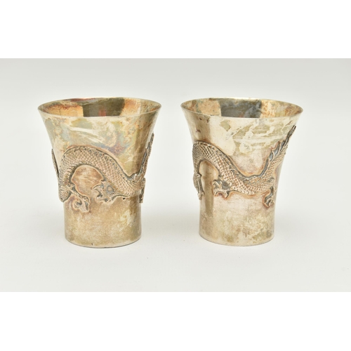 89 - A PAIR OF WHITE METAL ORIENTAL CUPS, each decorated with dragons, stamped to the base 'Silver', with... 