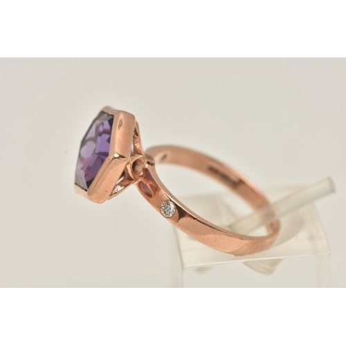 11 - A 9CT GOLD GEM SET RING, an elongated hexagon cut amethyst, bezel set in rose gold, flanked with two... 