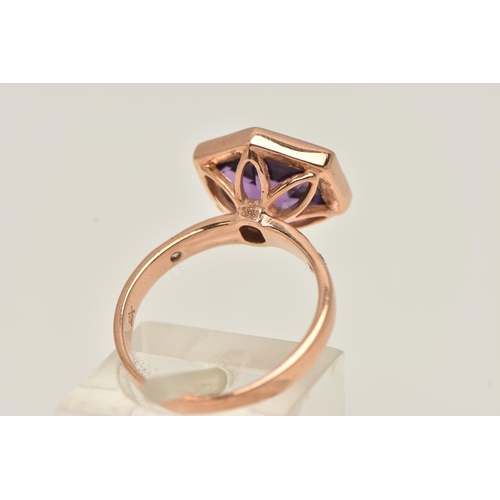 11 - A 9CT GOLD GEM SET RING, an elongated hexagon cut amethyst, bezel set in rose gold, flanked with two... 