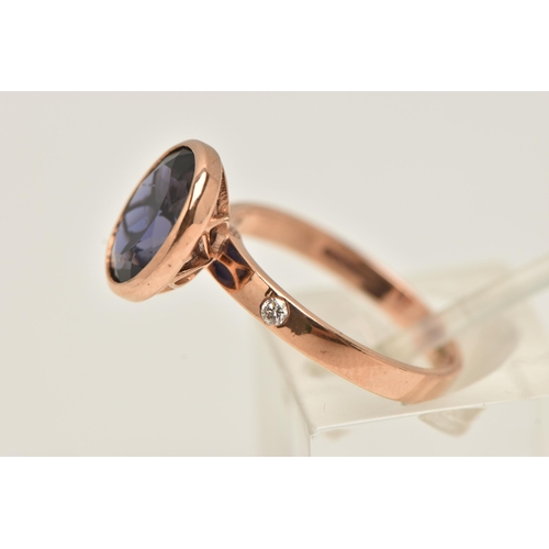 12 - A 9CT GOLD GEM SET RING, an oval cut blue stone assessed as iolite, bezel set in rose gold, flanked ... 