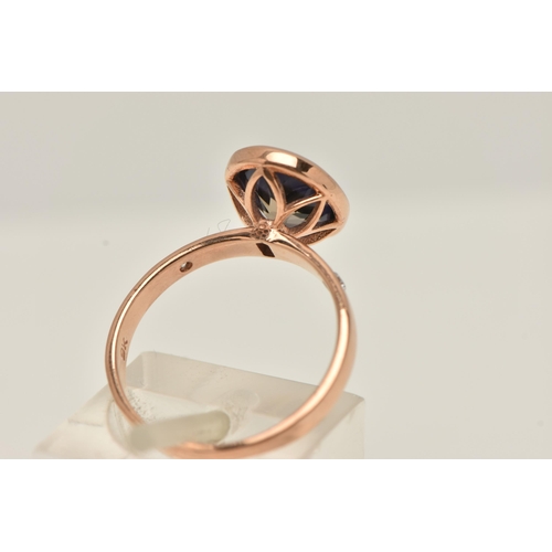 12 - A 9CT GOLD GEM SET RING, an oval cut blue stone assessed as iolite, bezel set in rose gold, flanked ... 