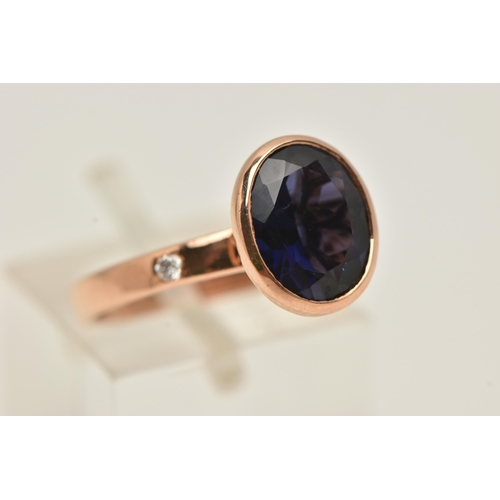12 - A 9CT GOLD GEM SET RING, an oval cut blue stone assessed as iolite, bezel set in rose gold, flanked ... 