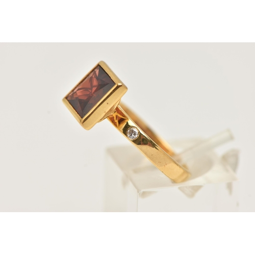 31 - A 9CT GOLD GEM SET RING, a square cut red stone assessed as garnet, bezel set in yellow gold, flanke... 