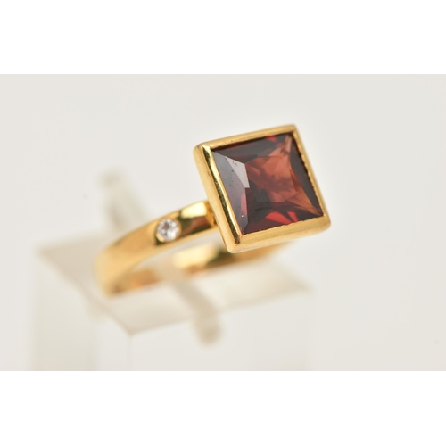 31 - A 9CT GOLD GEM SET RING, a square cut red stone assessed as garnet, bezel set in yellow gold, flanke... 