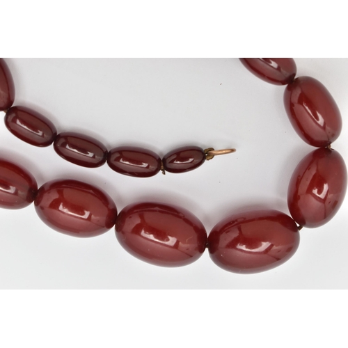 33 - A BAKELITE NECKLACE, twenty six cherry amber Bakelite oval beads, approximate length of largest bead... 