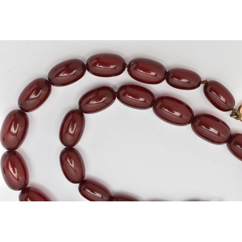 33 - A BAKELITE NECKLACE, twenty six cherry amber Bakelite oval beads, approximate length of largest bead... 