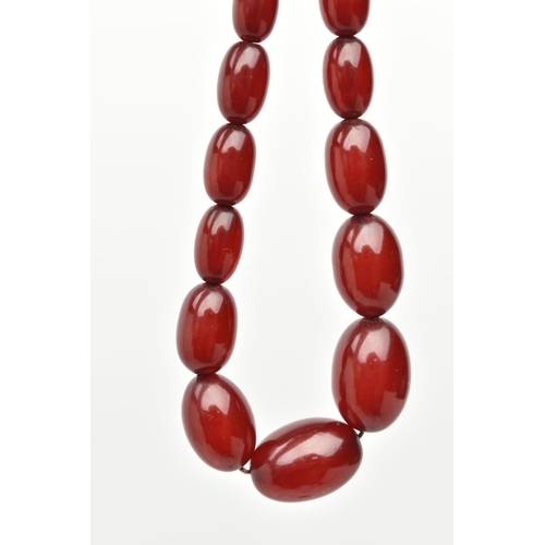 33 - A BAKELITE NECKLACE, twenty six cherry amber Bakelite oval beads, approximate length of largest bead... 