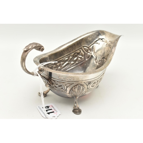 114 - AN IRISH GEORGE V SILVER SAUCE BOAT, with Celtic embossed design, raised on three shell capped feet,... 