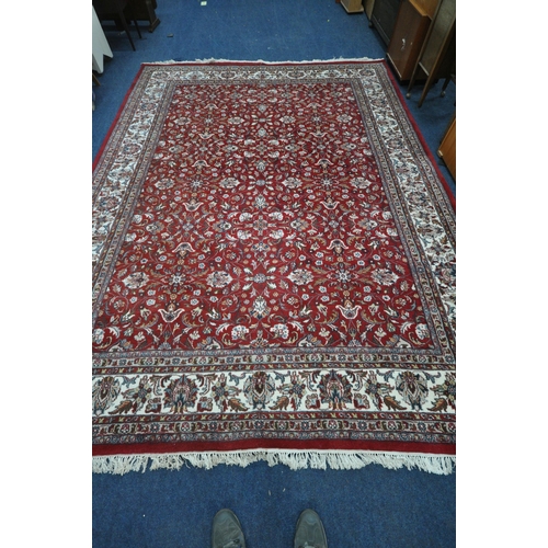 1218 - A LARGE RECTANGULAR RED GROUND WOOLLEN RUG, with repeating foliate patterns, surrounded by a multi-s... 