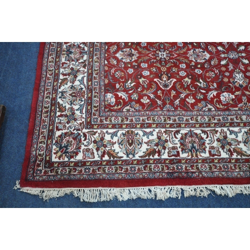 1218 - A LARGE RECTANGULAR RED GROUND WOOLLEN RUG, with repeating foliate patterns, surrounded by a multi-s... 