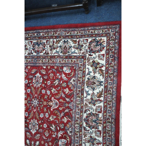 1218 - A LARGE RECTANGULAR RED GROUND WOOLLEN RUG, with repeating foliate patterns, surrounded by a multi-s... 