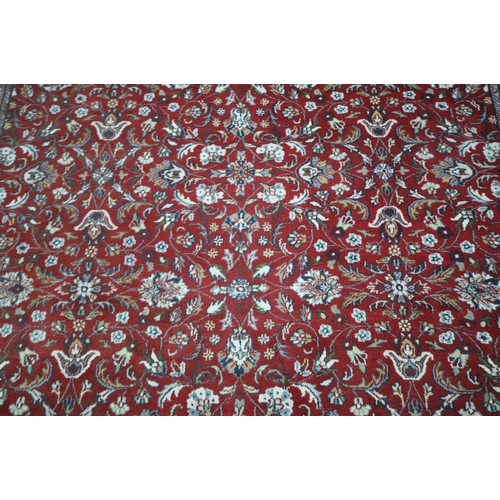 1218 - A LARGE RECTANGULAR RED GROUND WOOLLEN RUG, with repeating foliate patterns, surrounded by a multi-s... 