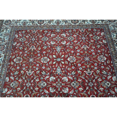 1218 - A LARGE RECTANGULAR RED GROUND WOOLLEN RUG, with repeating foliate patterns, surrounded by a multi-s... 