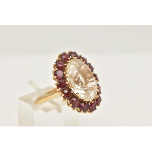 34 - A YELLOW METAL ROCK CRYSTAL AND GARNET CLUSTER RING, set with an oval shape rock crystal, measuring ... 