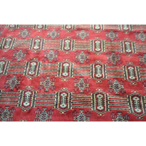 1320 - A LARGE MID TO LATE 20TH CENTURY WOOLLEN RUG, the repeating pattern surrounded by a multi strap bord... 