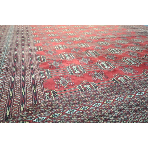 1320 - A LARGE MID TO LATE 20TH CENTURY WOOLLEN RUG, the repeating pattern surrounded by a multi strap bord... 