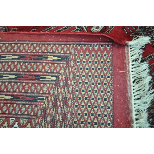 1320 - A LARGE MID TO LATE 20TH CENTURY WOOLLEN RUG, the repeating pattern surrounded by a multi strap bord... 