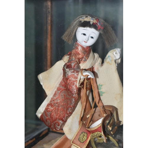 358 - A JAPANESE COSTUME DOLL IN A GLAZED CASE, the vintage female doll wearing a kimono and holding a sam... 