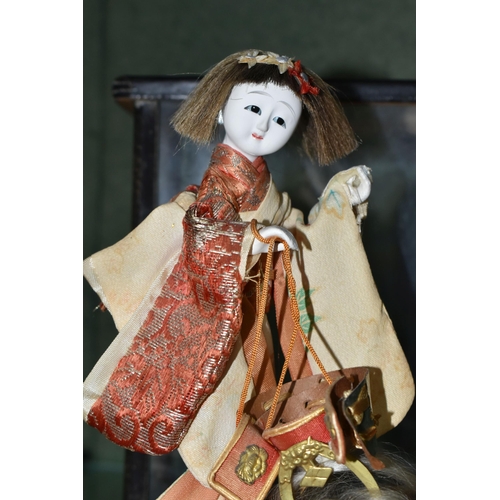 358 - A JAPANESE COSTUME DOLL IN A GLAZED CASE, the vintage female doll wearing a kimono and holding a sam... 