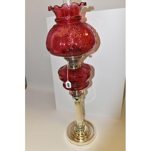 494 - A VICTORIAN STYLE CRANBERRY COLOURED GLASS OIL LAMP, with circular silver coloured Corinthian column... 