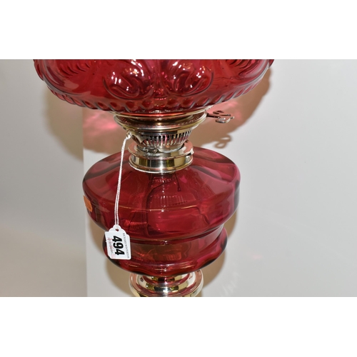 494 - A VICTORIAN STYLE CRANBERRY COLOURED GLASS OIL LAMP, with circular silver coloured Corinthian column... 