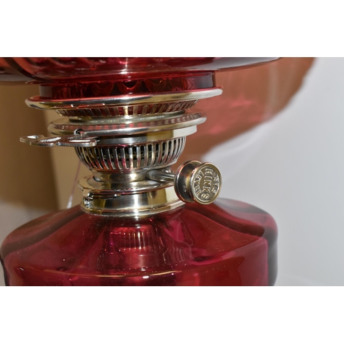 494 - A VICTORIAN STYLE CRANBERRY COLOURED GLASS OIL LAMP, with circular silver coloured Corinthian column... 