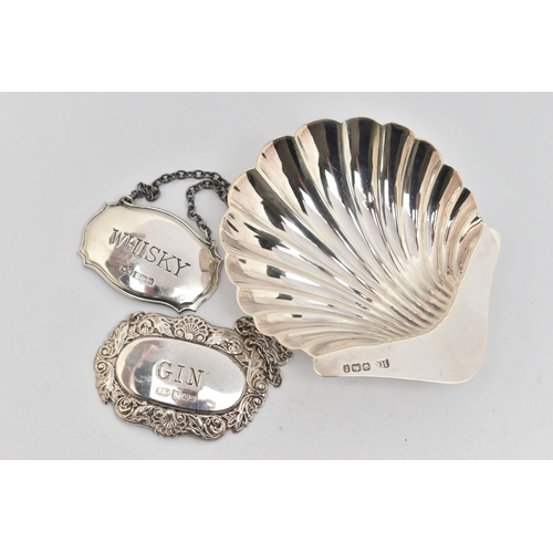 170 - A SILVER SHELL SHAPE DISH AND TWO DECANTER LABELS, the shell shape dish raised on three ball feet, h... 