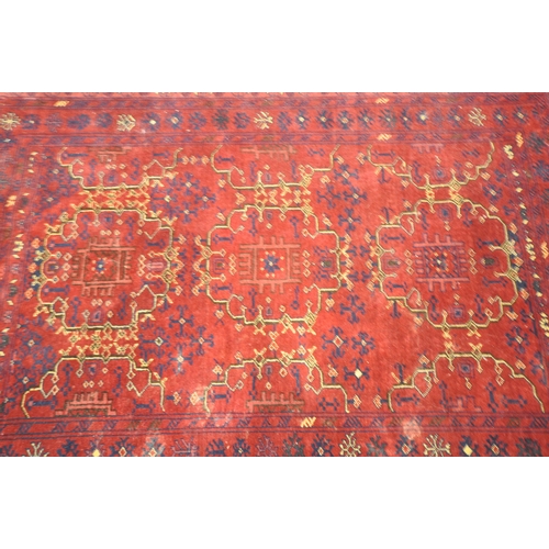 1280 - A RED GROUND RECTANGULAR WOOLEN RUG, with repeating geometric patterns, surrounded by a multi-strap ... 